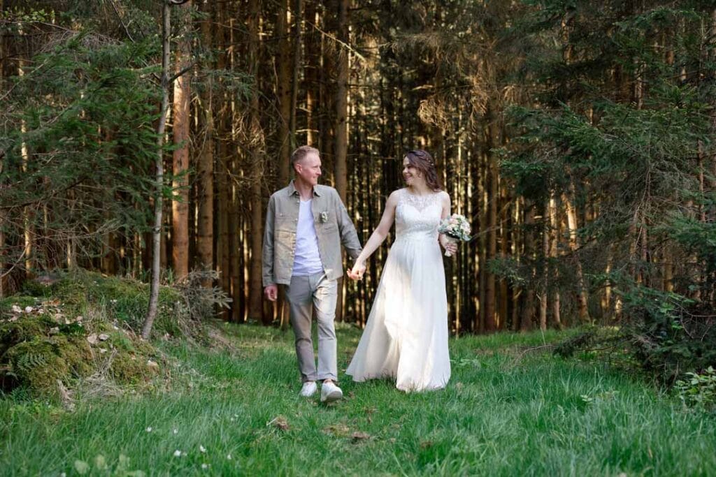 Brautpaar beim Spaziergang im Wald, Hand in Hand, romantische Hochzeitsfotos im Grünen.