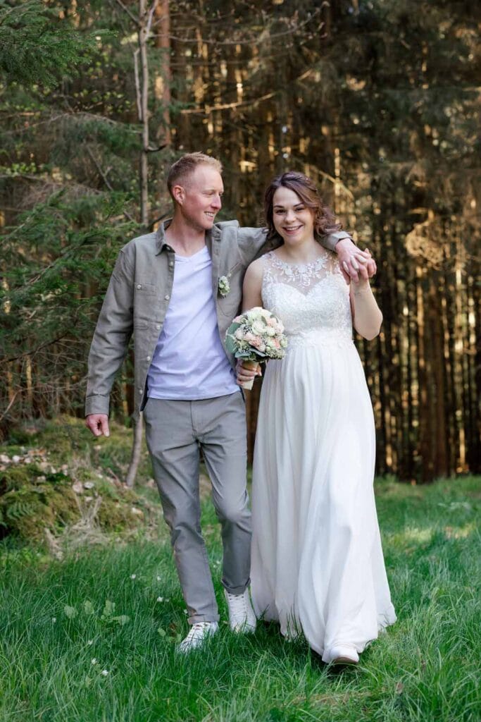 Fröhliches Brautpaar bei Waldspaziergang, lachend und verliebt, im Grünen, natürliche Hochzeitsfo.