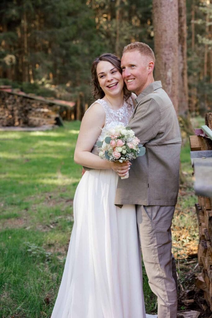 Fröhliches Brautpaar bei einer emotionalen Hochzeit im Grünen, umgeben von Bäumen und Natur.