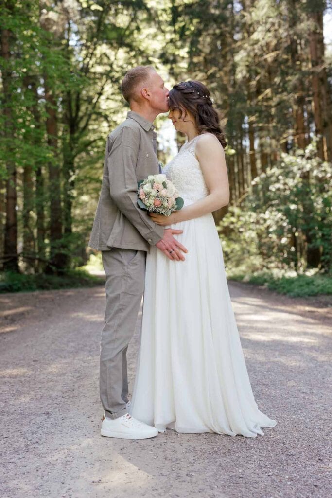 Brautpaar im Wald, romantisches Hochzeitsfoto, Kuss, Natur, Liebe, emotionale Fotografie.