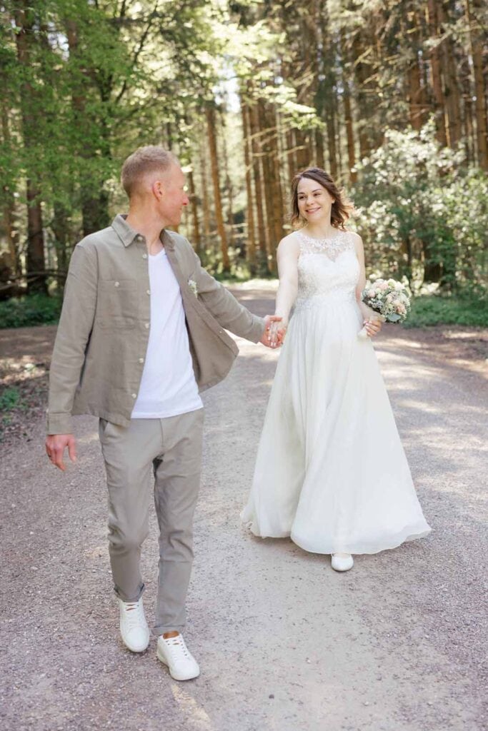 Brautpaar im Wald bei Sonnenlicht, Hand in Hand, natürliche Hochzeitsfotografie.