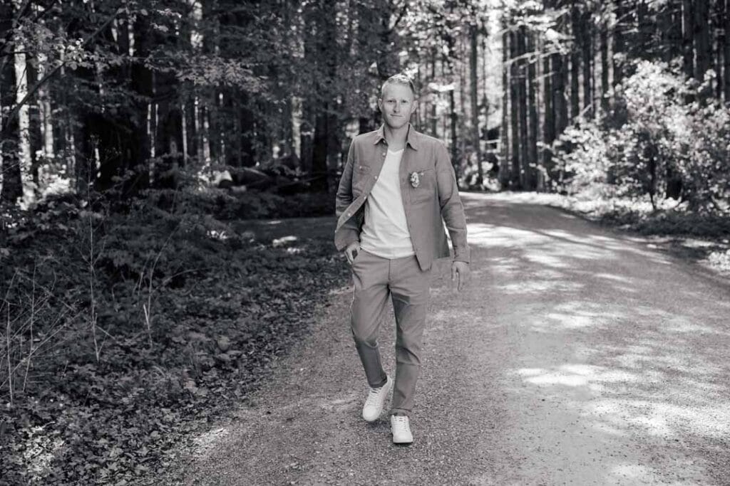 Junger Mann beim Spaziergang im Wald, entspannt und stilvoll, in natürlicher Umgebung.
