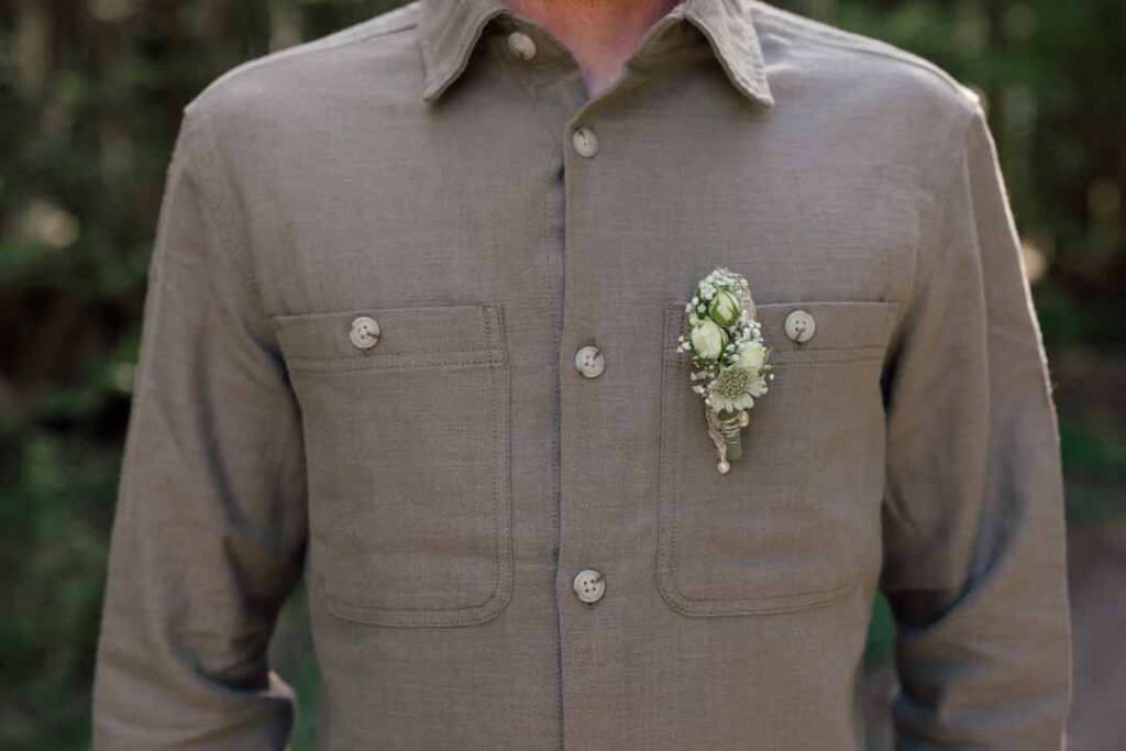 Nahaufnahme eines Hochzeitsanzugs mit Blumenbrosche am Revers, detailreiche Textur.