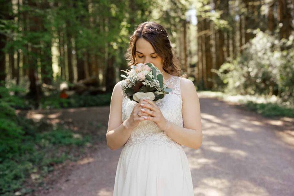 Braut mit Blumenstrauß im Wald, natürliche Hochzeitsaufnahme.