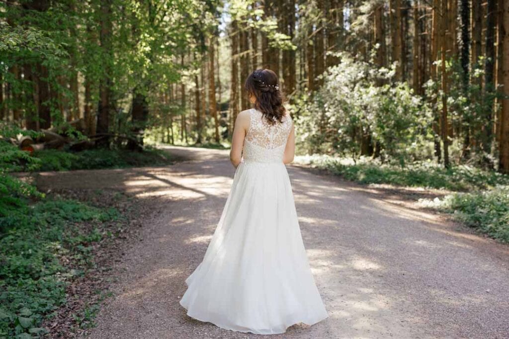 Braut im weißen Hochzeitskleid auf Waldweg, Natur, Sonnenlicht, romantisch.