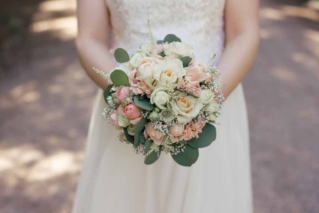 Hochzeitsstrauß mit weißen und rosa Blumen, gehalten von einer Braut in einem weißen Kleid.