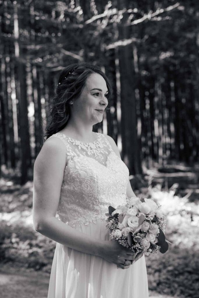 Braut im Wald mit Blumenstrauß, natürliche Hochzeitsfotografie, emotionales Brautpaarshooting.