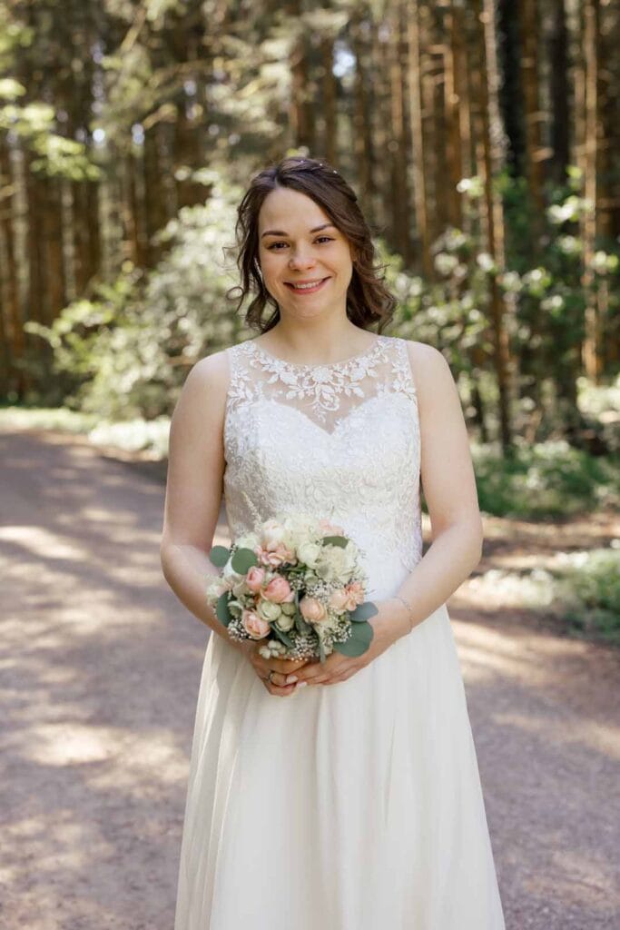 Hochzeitsbraut im Wald mit Blumenstrauß, authentische und emotionale Hochzeitsfotografie im Freien.
