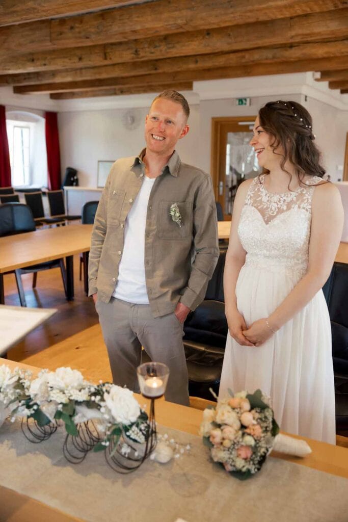 Hochzeitspaar während der Zeremonie, lachend und glücklich, im festlichen Raum mit Holzdecke.