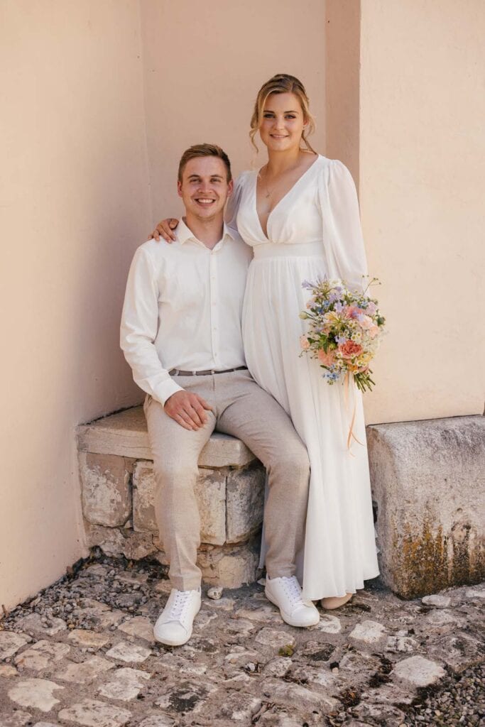 Lächelndes Hochzeitspaar in weißen Outfits, fotografiert von Saskia Römer – Fotografie mit Herz Laug.