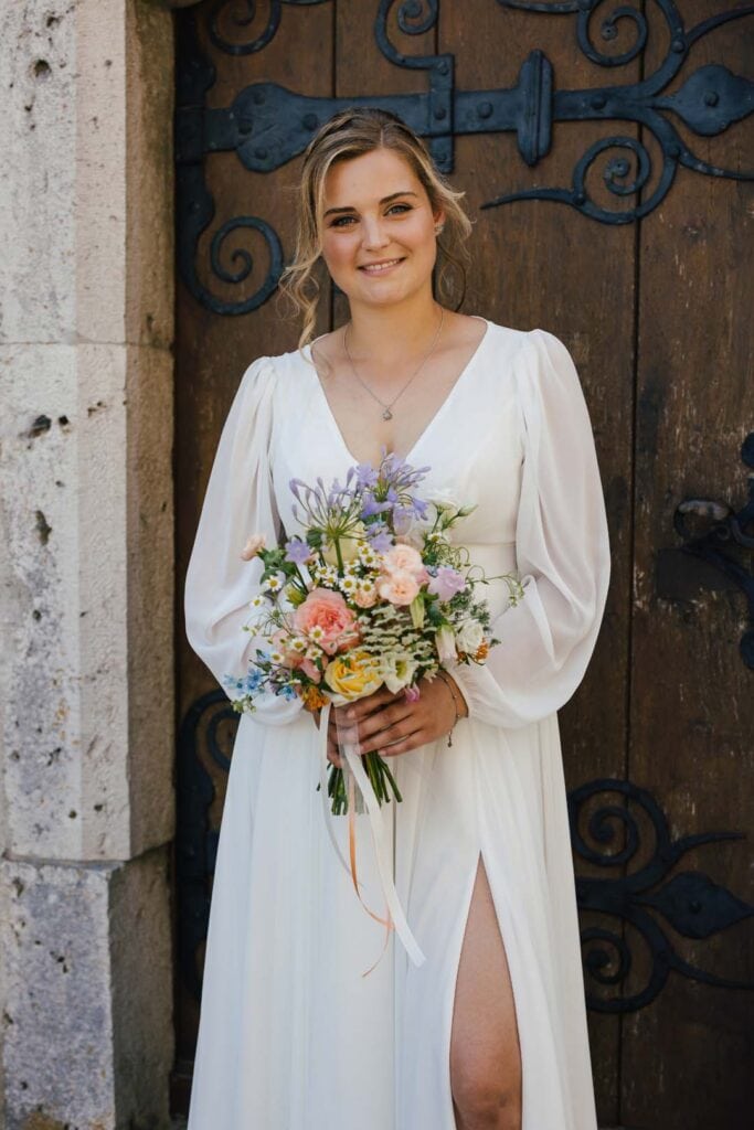 Braut in weißem Kleid mit Blumenstrauß vor historischem Tor in Lauingen.