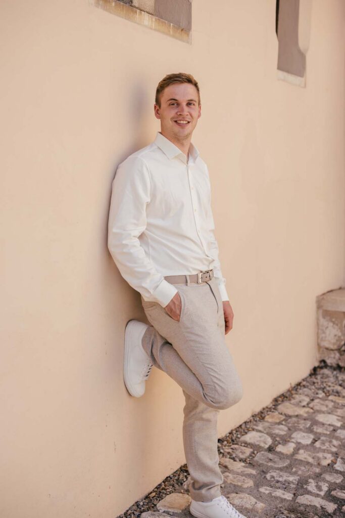 Junger Mann in weißem Hemd und grauen Hosen lehnt an Wand in Lauingen.